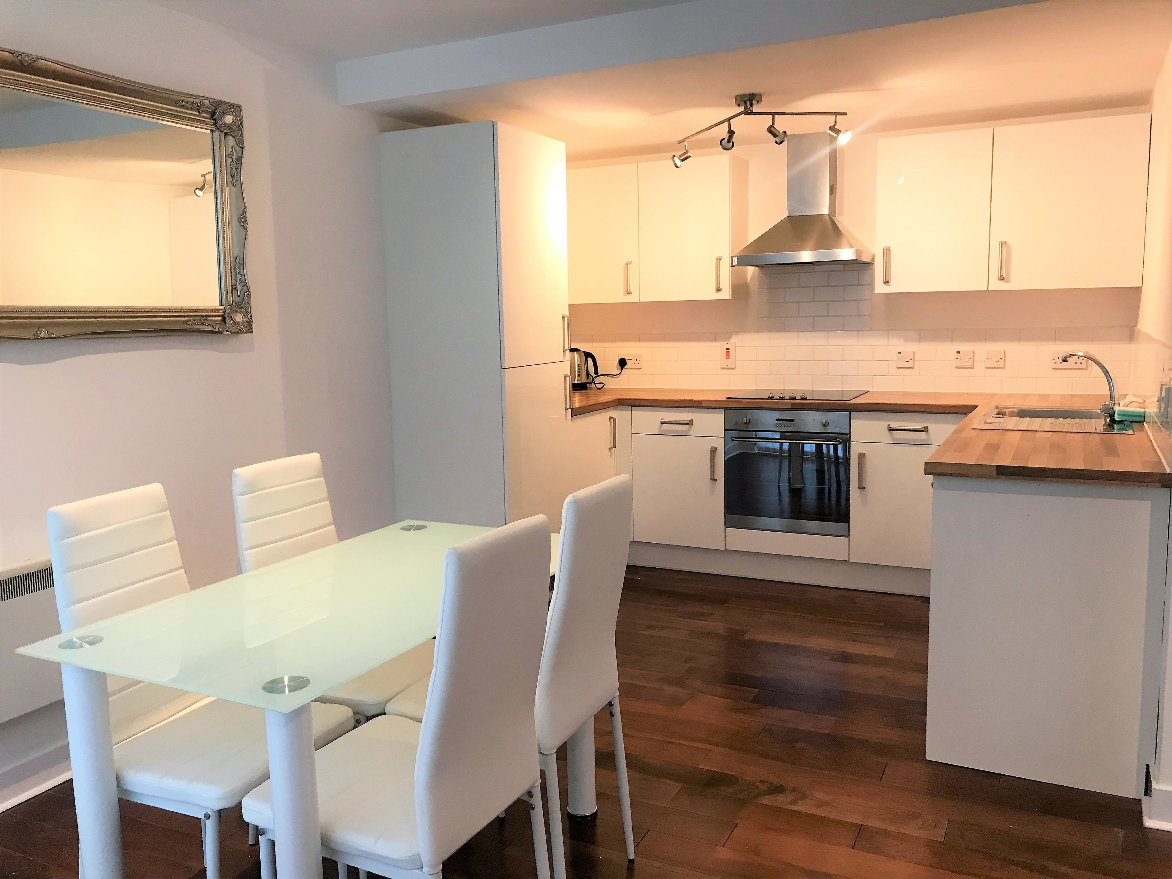 A modern kitchen with white cabinets, a stainless steel oven, and a glass dining table with white chairs.