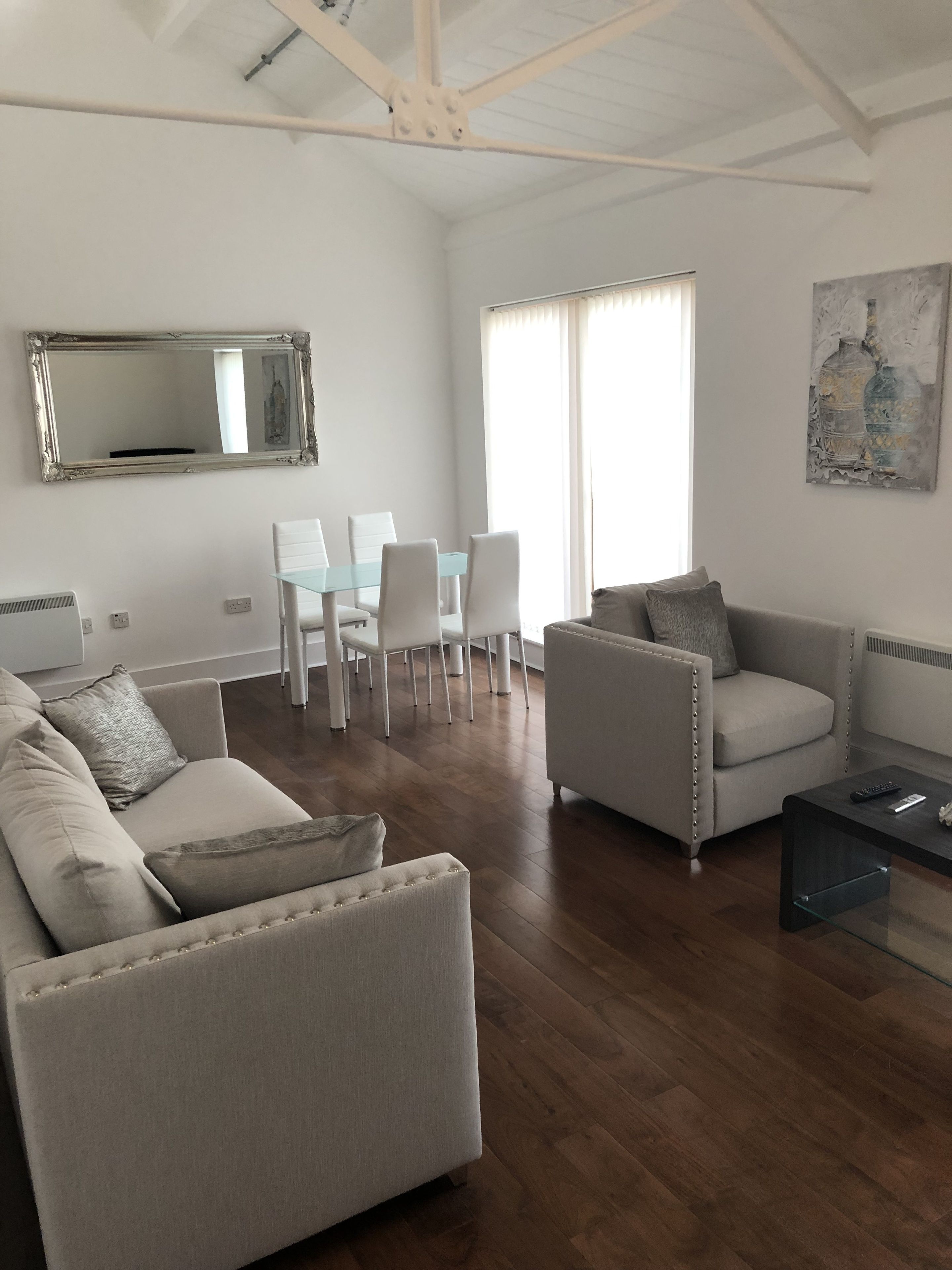 A modern living room with a dining area, featuring a large mirror, a painting, and a sofa set.