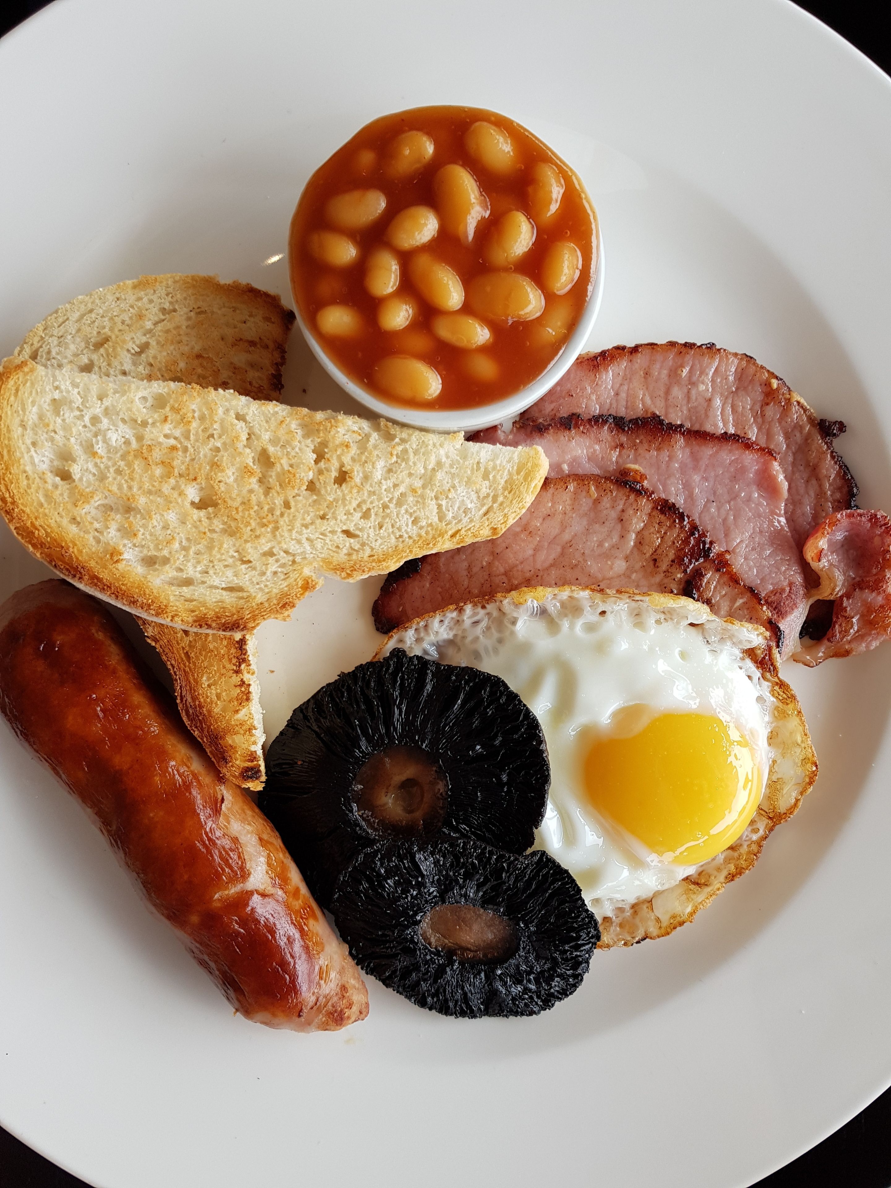 Une assiette garnie de tranches de jambon, d’un œuf au plat, de saucisses, de pain grillé et de haricots cuits.