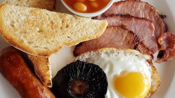 A plate with slices of ham, a fried egg, sausages, toast, and baked beans.