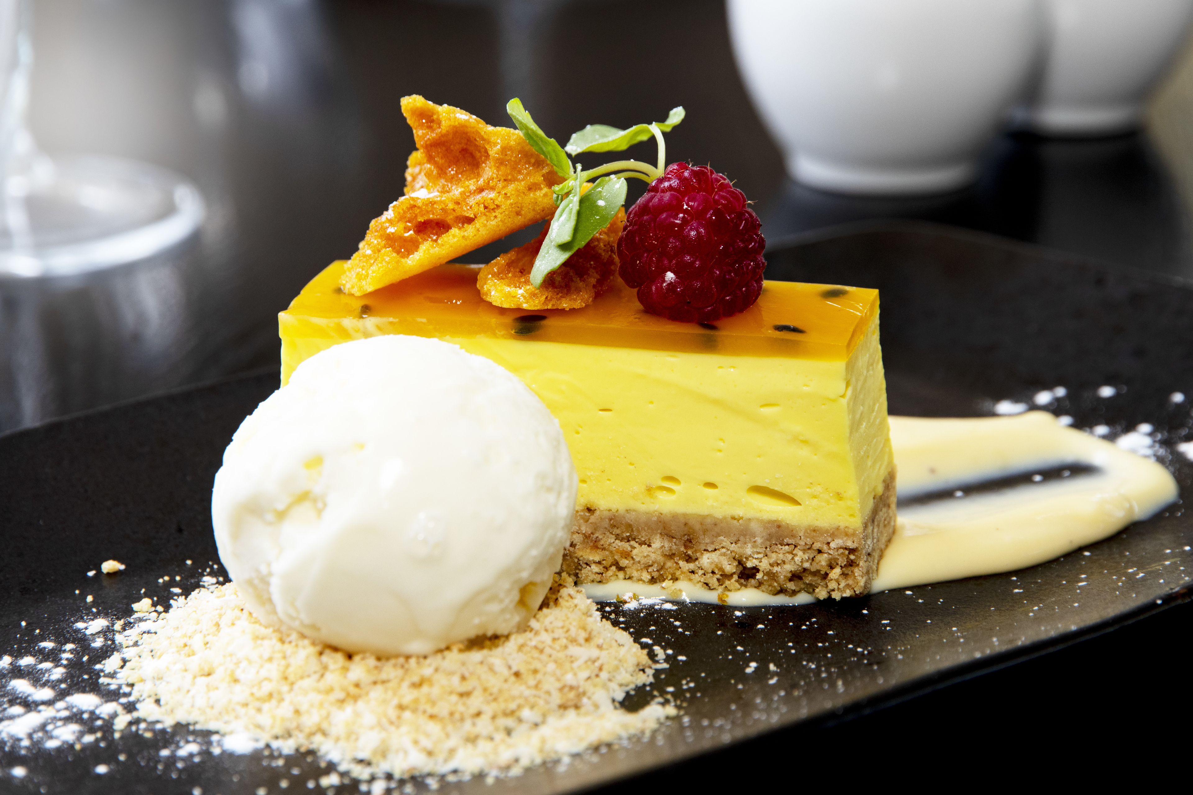A dessert plate with a slice of cheesecake, a scoop of vanilla ice cream, and a raspberry.