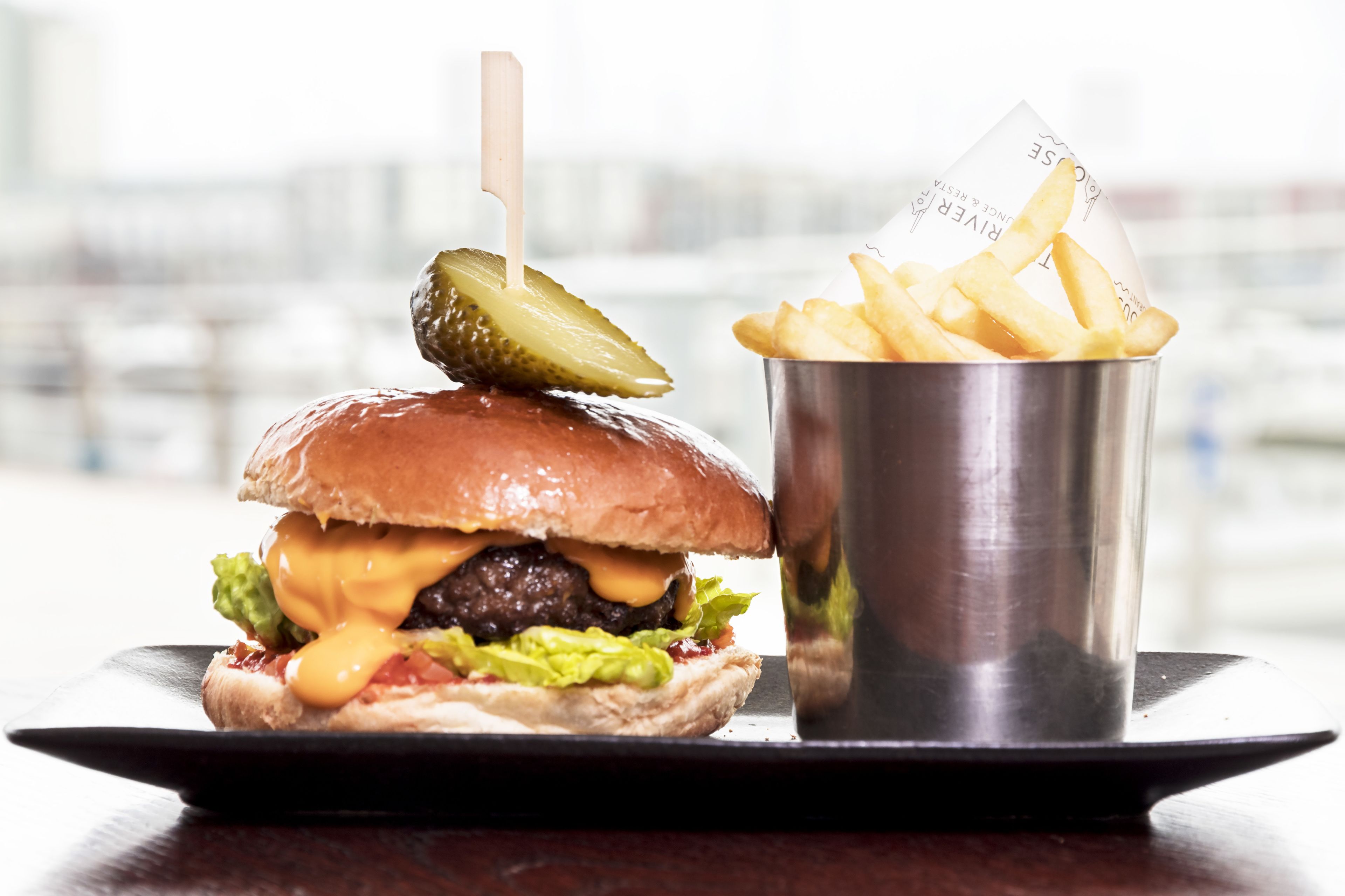 En hamburgare med en inlagd gurka ovanpå och en portion pommes frites på en svart tallrik.