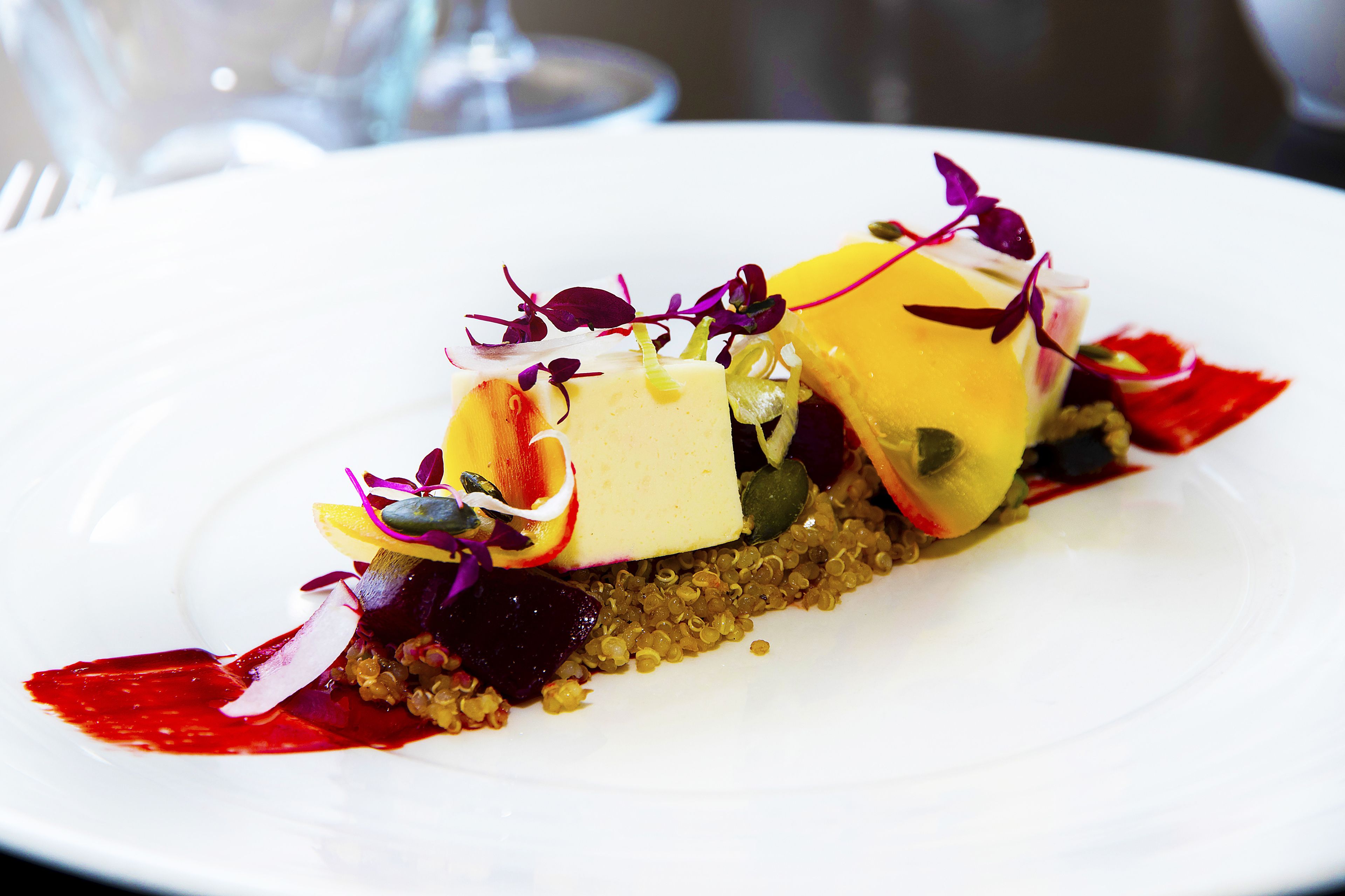 A white plate with a colorful food arrangement, including yellow and red elements, possibly cheese, and garnishes.