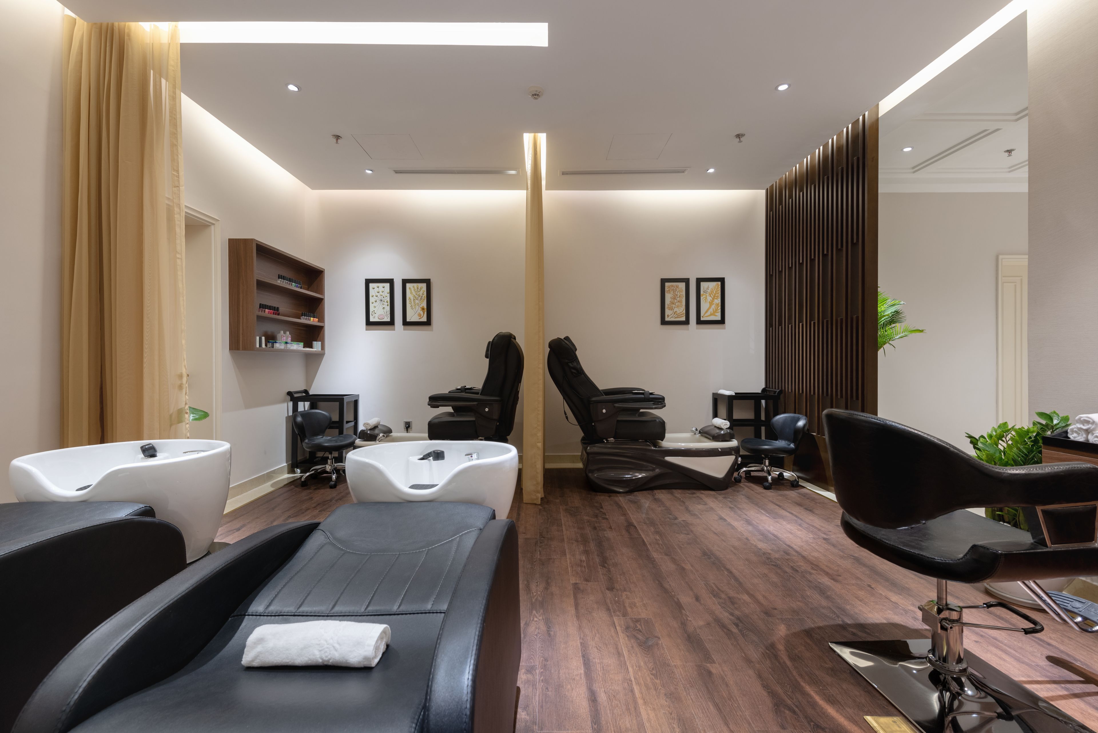 A modern spa room with a massage table, two massage chairs, a small reception desk, and a large mirror.