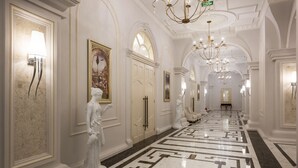 A grand hallway with marble flooring, classical statues, and ornate chandeliers.