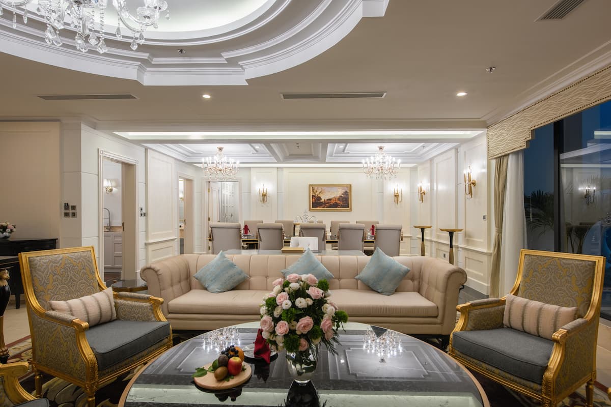Una sala de estar lujosa con un sofá grande color beige, dos sillones ornamentados, una mesa de centro de cristal y un centro de mesa floral.