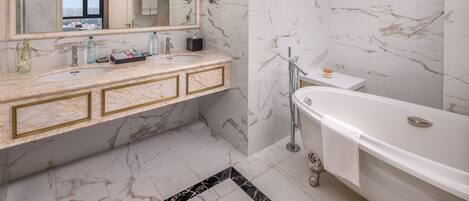 A bathroom with marble walls and a large mirror, a double sink vanity, a bathtub, and a view through the window.