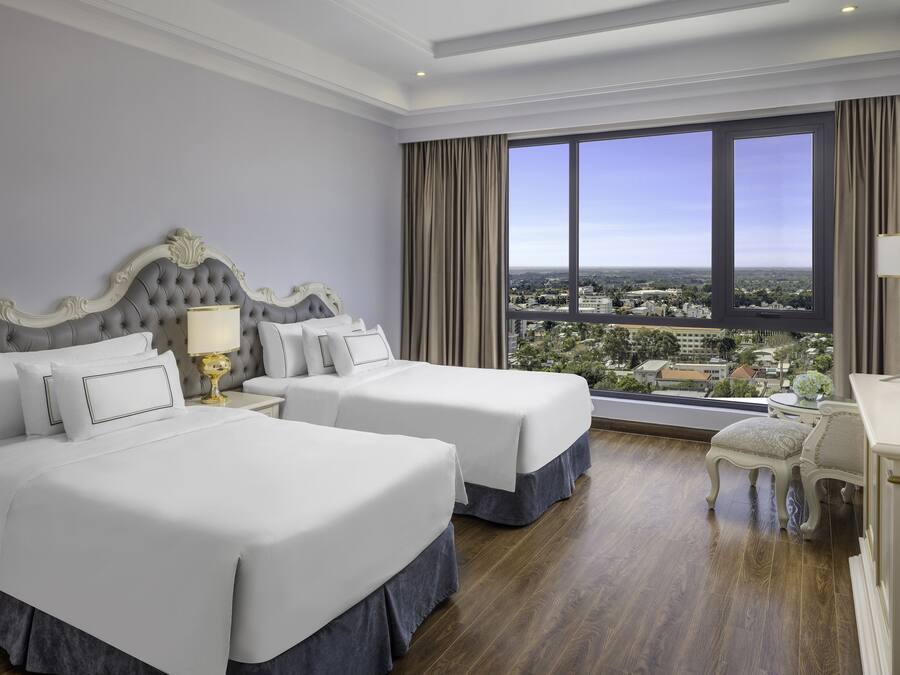 Habitació d'hotel amb dos llits, una finestra gran amb vista a la ciutat, una taula de treball amb una cadira i una televisió.