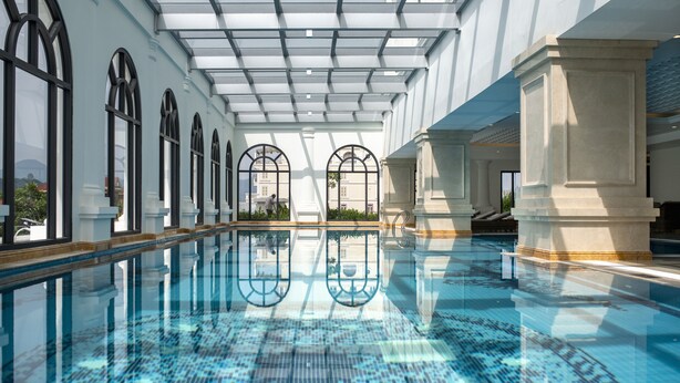 A large indoor swimming pool with clear blue water, arched windows, and a high ceiling with skylights.