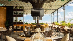 An outdoor dining area with wicker furniture, tables set with glassware, and potted plants.