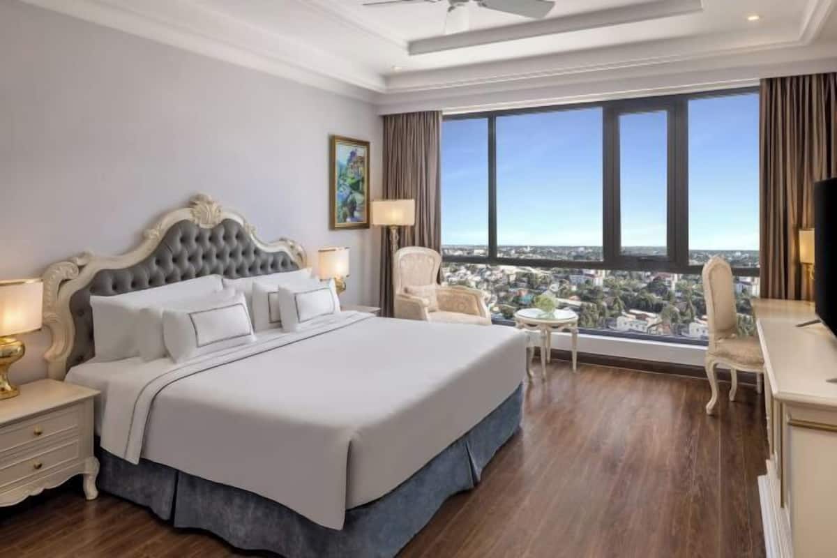 Habitación de hotel con una cama grande, un escritorio, una silla, televisión y vistas a la ciudad.