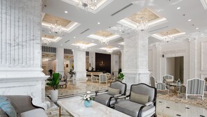 A spacious lobby with marble columns, elegant chandeliers, and a central seating area with sofas and armchairs.
