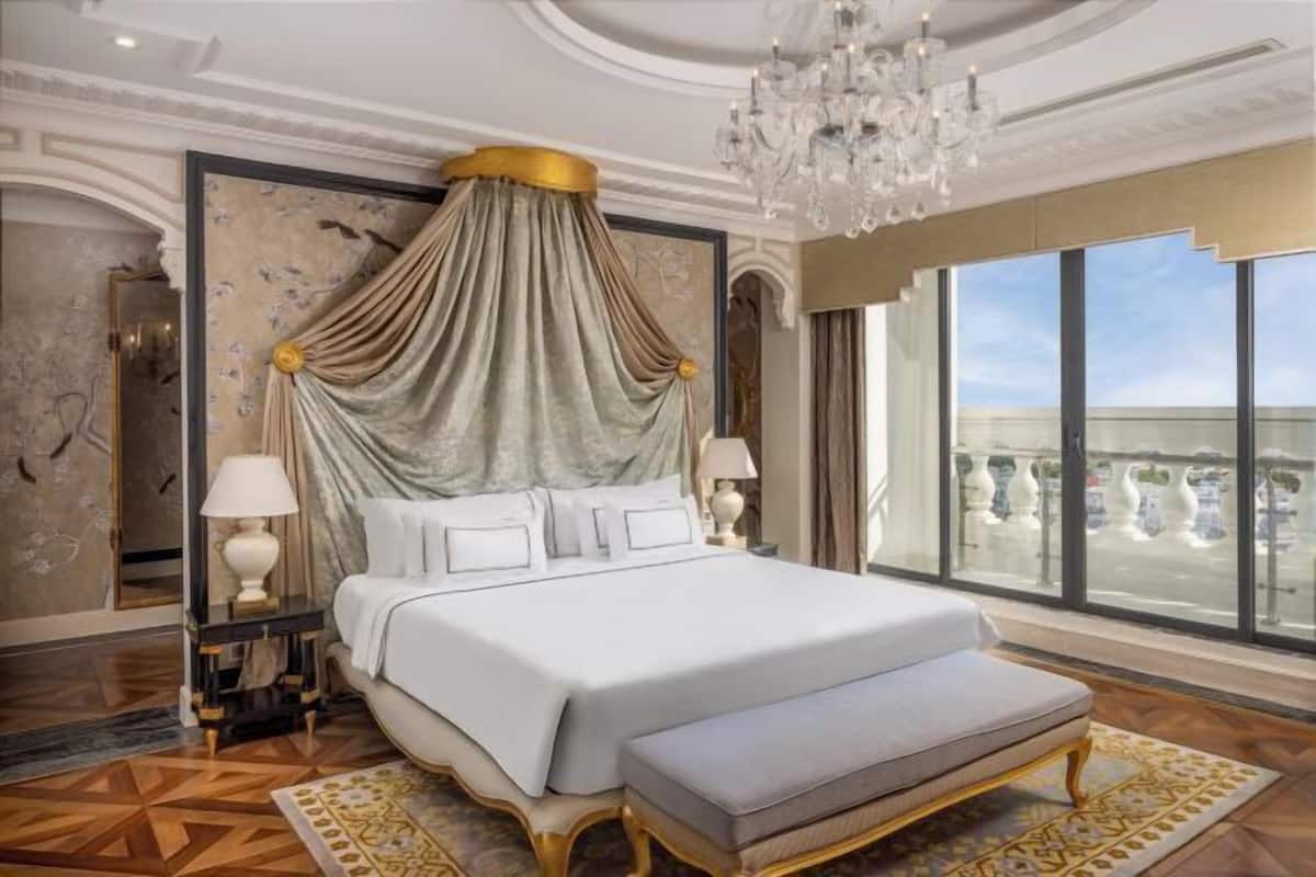Una cama grande con dosel, dos lámparas de noche, un banco y un ventanal con vistas.