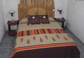 A neatly made bed with a patterned bedspread, two bedside tables with lamps, and a headboard. - Apto Ricardo (Varadero)