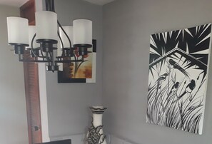 A room with a modern chandelier, a framed painting of birds, and a decorative vase. - Apto Ricardo (Varadero)