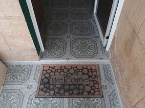 A welcome mat with the word "Welcome" on a patterned floor and a door leading to a room. - Apto Ricardo (Varadero)