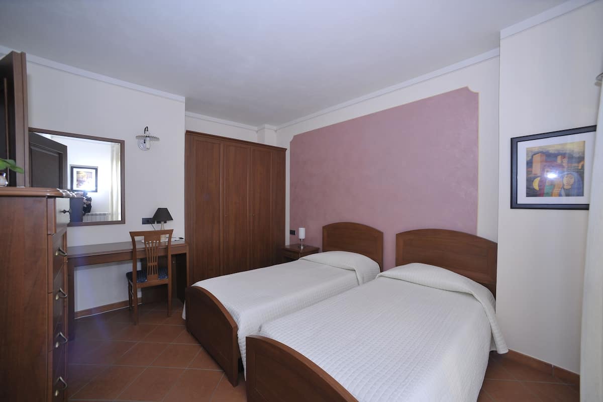 Un dormitorio con dos camas individuales, un escritorio, una silla, un armario y un espejo.