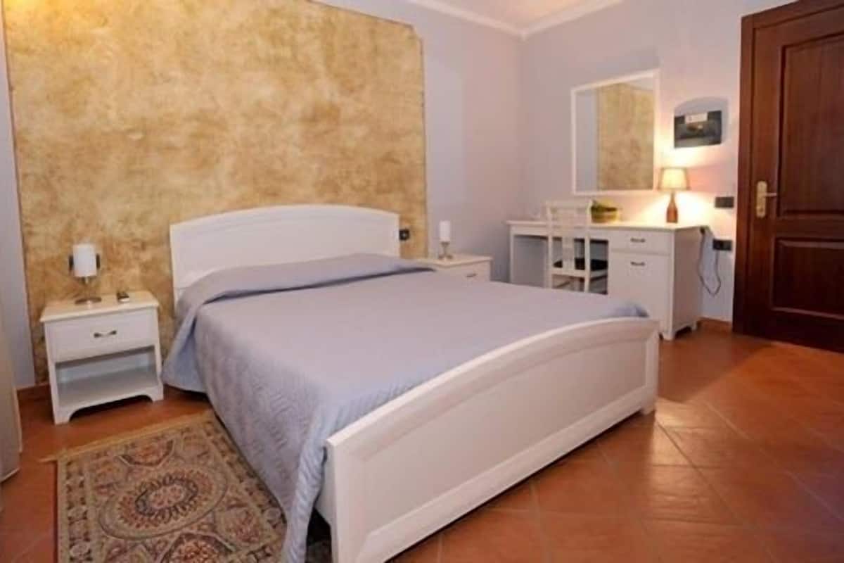 Un dormitorio con cama, mesitas de noche, cómoda, espejo y puerta.