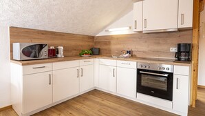 A compact kitchen with white cabinets, a microwave, a coffee maker, a sink, and an oven. - Alphirt Ferienwohnungen (Fischen im Allgaeu)