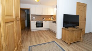 A compact kitchen with white cabinets, a built-in oven, and a coffee maker. A flat-screen TV is on a wooden stand. - Alphirt Ferienwohnungen (Fischen im Allgaeu)