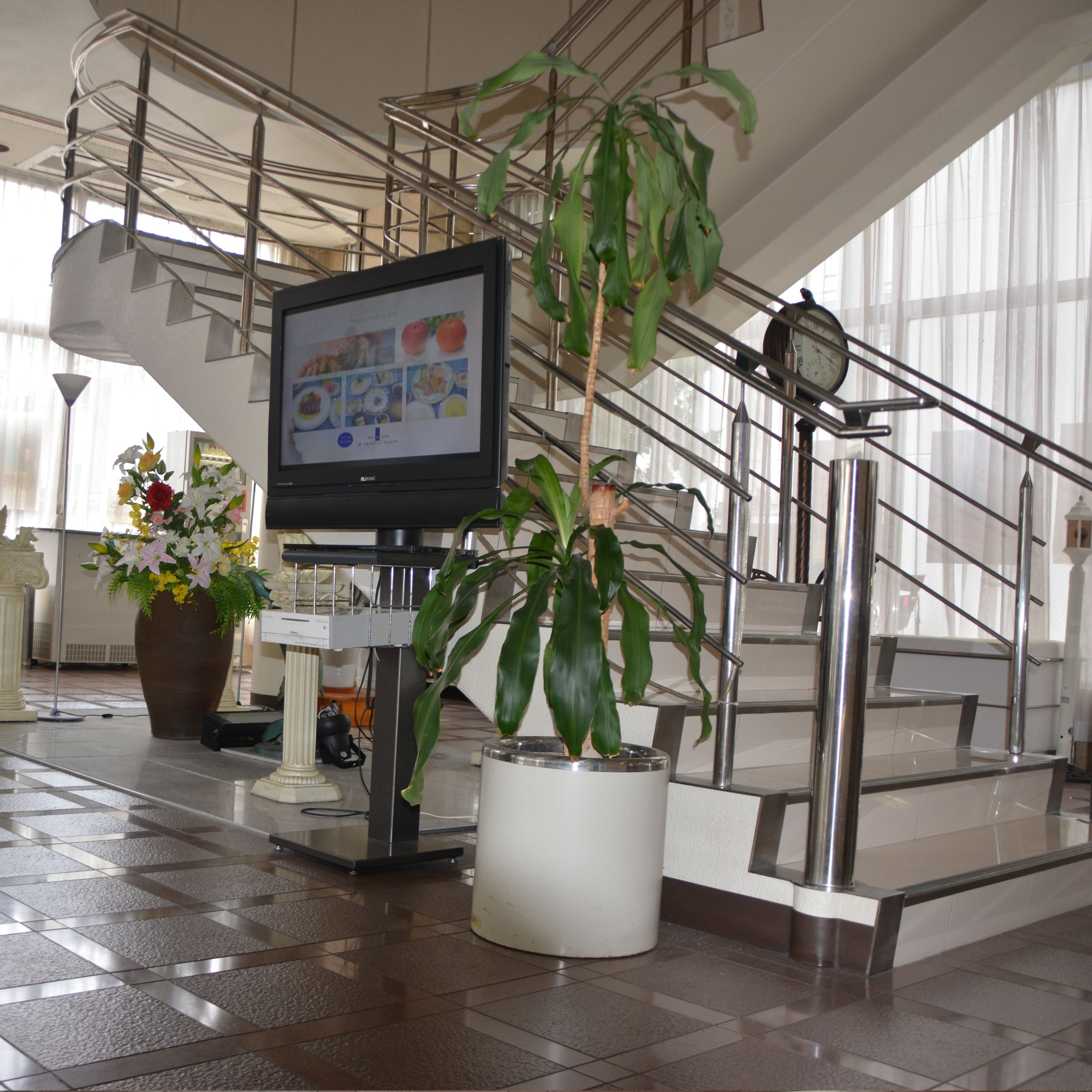 A lobby with a large screen displaying food images, a potted plant, and a staircase.
