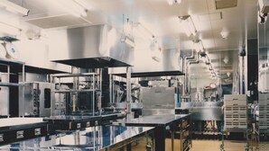 Een professionele keuken met roestvrijstalen apparatuur, een lange werkbladen en verlichting boven het werkgebied.