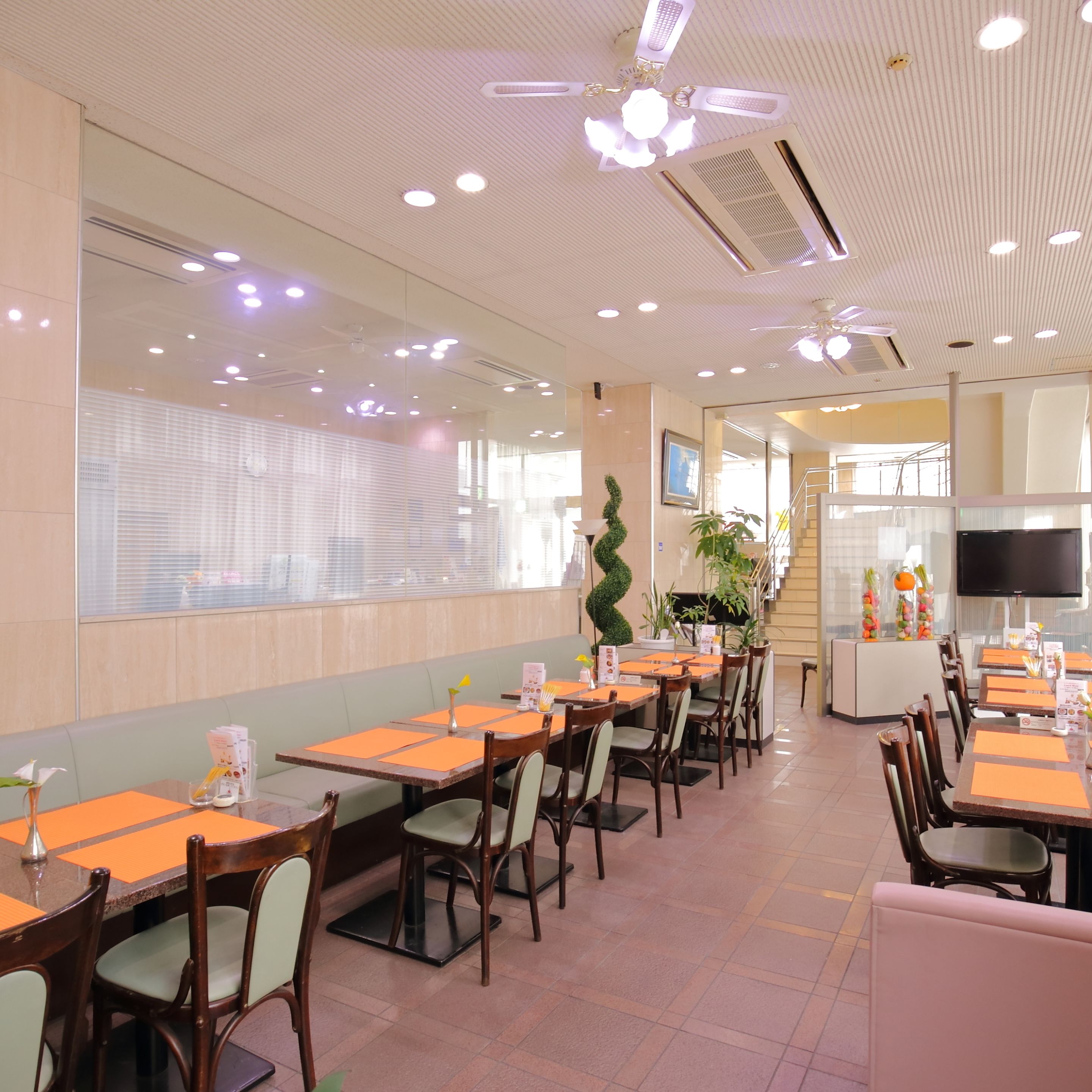 A restaurant with multiple dining tables and chairs, a ceiling fan, and a TV screen.