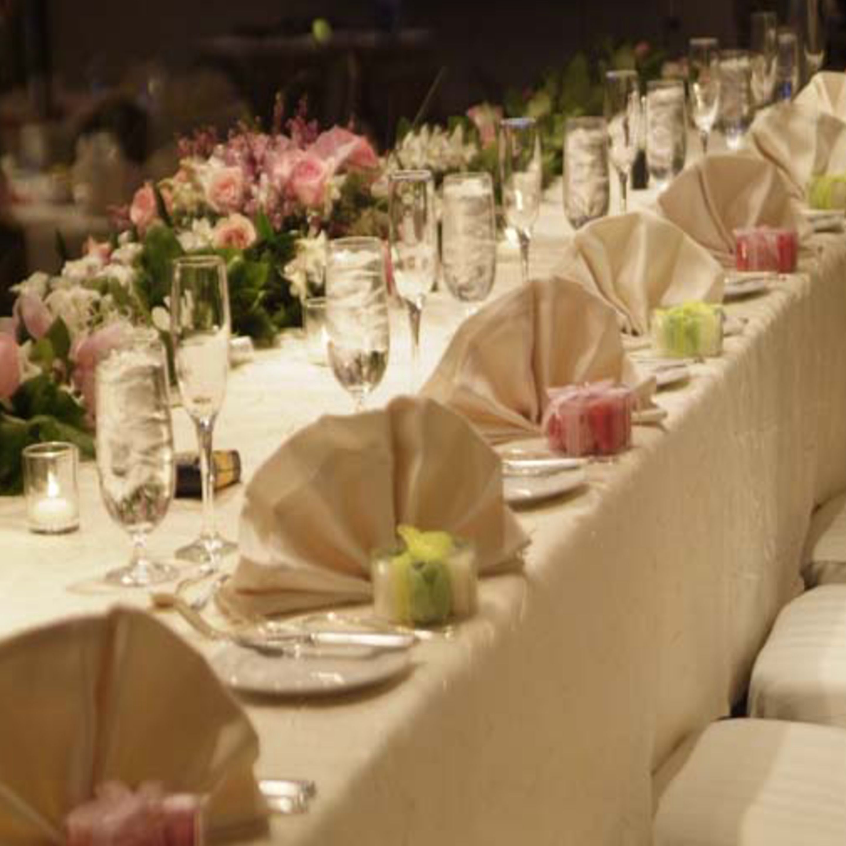 A banquet table set with glassware, plates, and napkins, surrounded by floral arrangements.