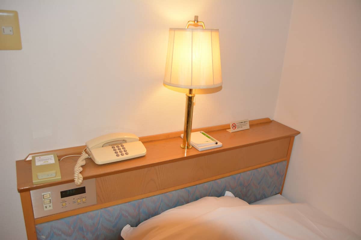 Habitació d'hotel amb una taula de nit que té una làmpada, un telèfon i un full de paper.