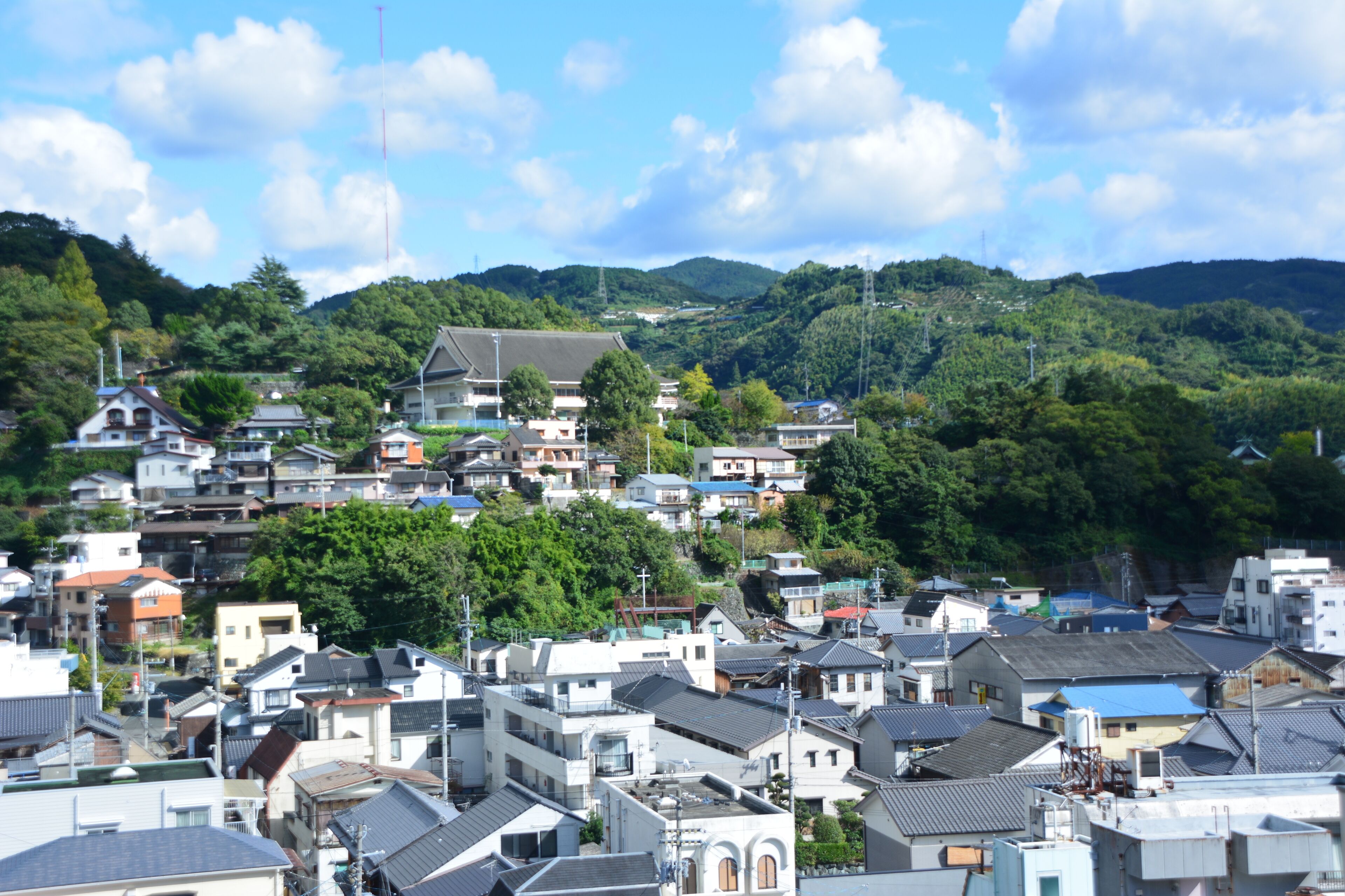 A residential area with houses on a hillside, surrounded by greenery.