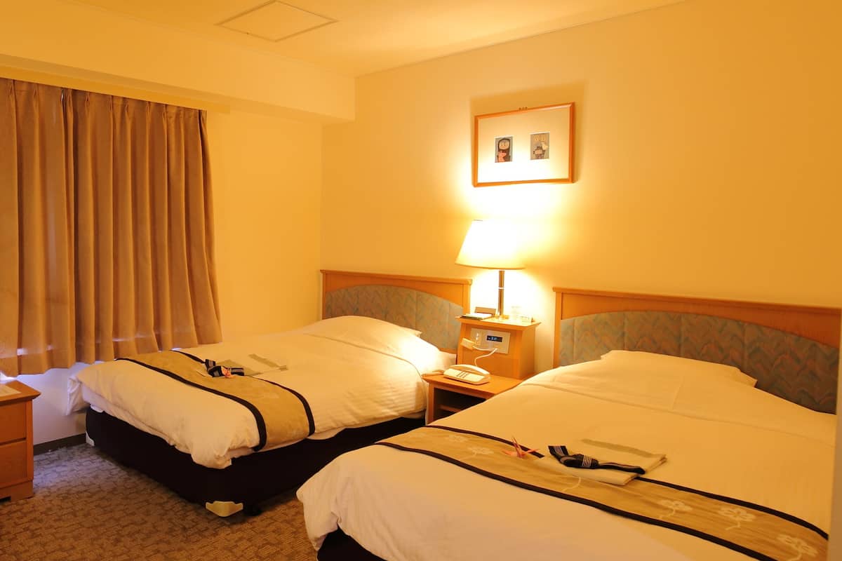 Habitació d'hotel amb dos llits, una tauleta de nit amb una làmpada, un telèfon i un quadre al mur.