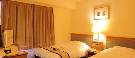 A hotel room with two beds, a desk with a telephone, and a bedside table with a lamp.