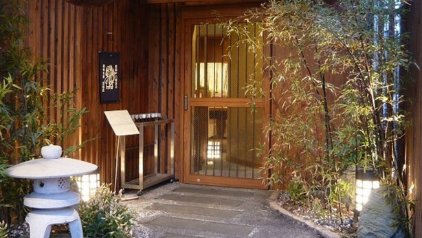 Een houten gebouw met een traditionele Japanse inkom, een pad van stenen en een kleine stenen lantaarn.