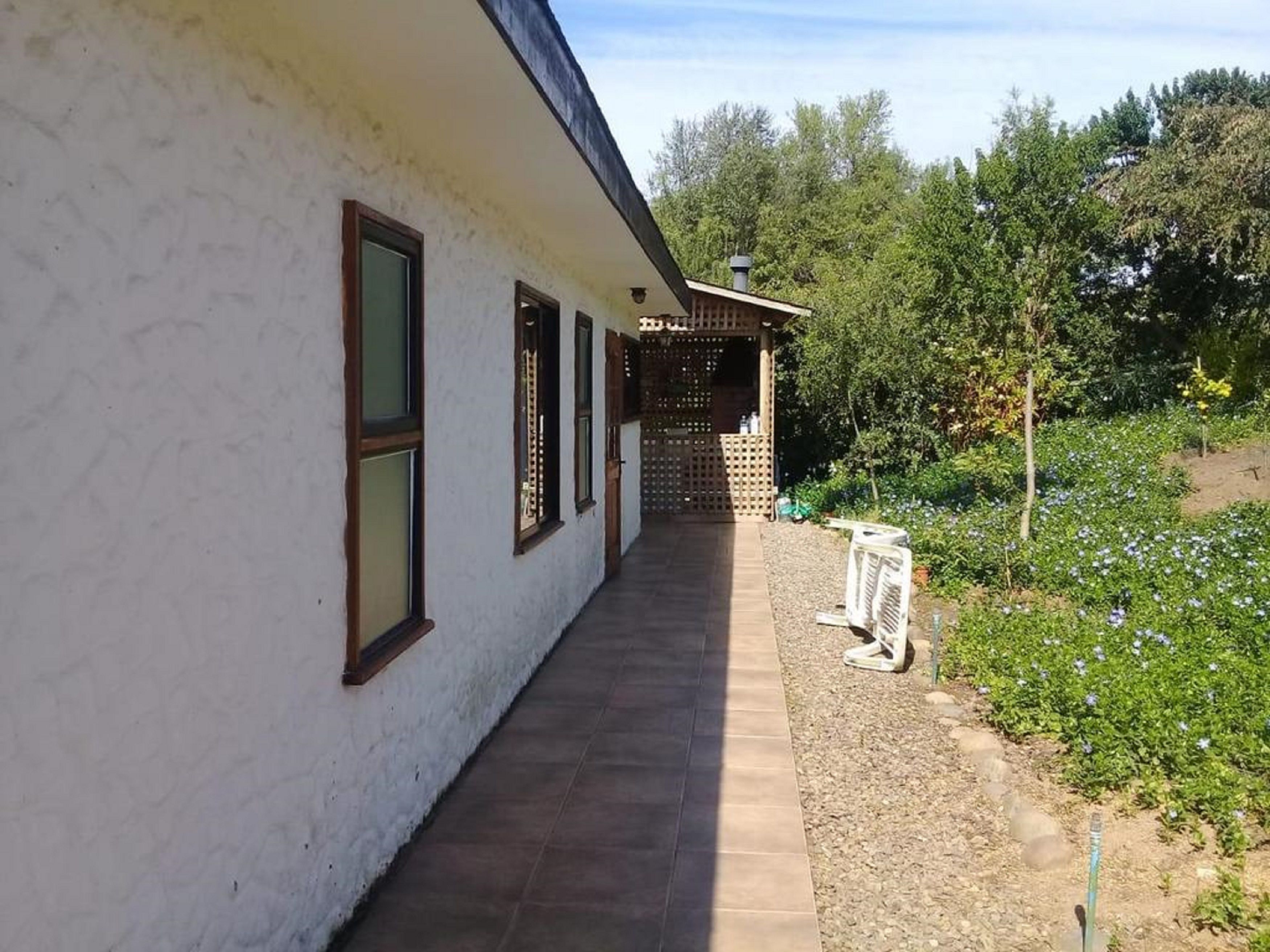 A covered walkway leading to a wooden structure with a view of a garden with flowers and trees.