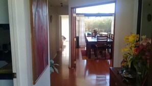 A hallway leading to a dining area with a wooden table and chairs, a potted plant, and a vase of flowers. - Casa en Condominio Terramar Maitencillo (Puchuncavi)