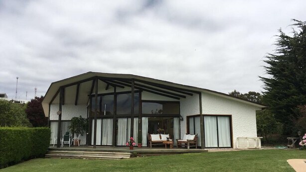 A modern house with a large glass window, a covered porch, and a well-maintained lawn. - Casa en Condominio Terramar Maitencillo (Puchuncavi)