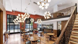 Un espacio interior amplio con piso de madera, varios arreglos de asientos y una escalera con barandillas ornamentales.