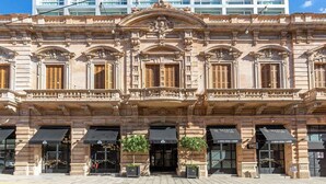 Un edificio histórico con arquitectura ornamentada, varias tiendas en la planta baja y un moderno rascacielos al fondo.