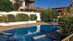 A swimming pool with a wooden deck, surrounded by a white wall and greenery. - Departamento Mares de Concon (Concon)