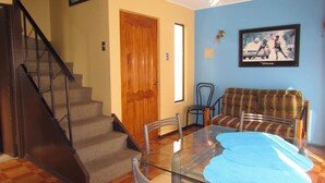 Un salon avec un escalier, une porte en bois, un mur bleu, un canapé à carreaux et une table en verre.