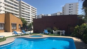 Une piscine entourée de chaises longues et d’une table, le tout délimité par un mur de briques et avec des bâtiments en arrière-plan.