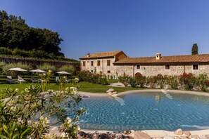 A pool area with lounge chairs and a stone building in the background. - Villa Padovani (Pastrengo)