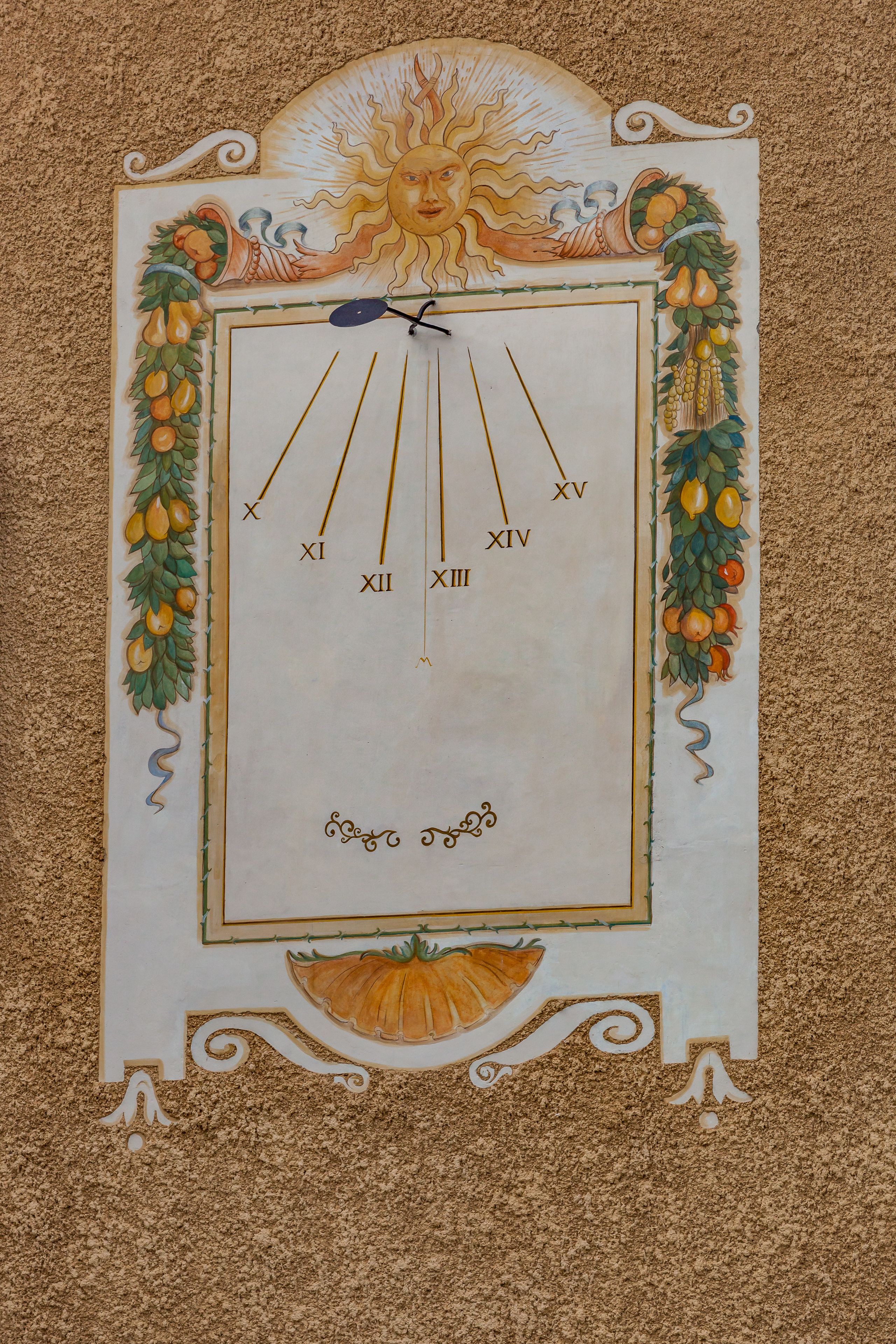 Un mur orné d’une horloge décorative représentant un soleil et des motifs de fruits.