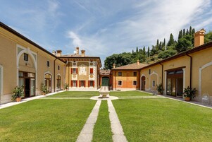 Un cortile con fontana al centro, circondato da edifici con porte e finestre ad arco.
