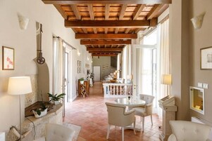 Un'ampia sala con soffitto in legno, una zona pranzo con tavolo e sedie, e una cucina sullo sfondo.