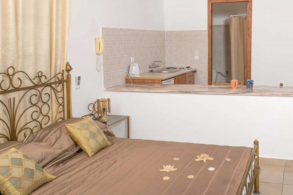 A bedroom with a bed, a bedside table with a lamp, a small bathroom with a sink and mirror, and a telephone on the wall.
