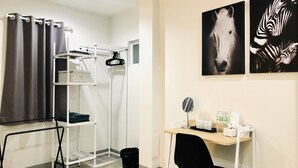 Une pièce comprenant un bureau, une chaise et un étendoir à linge. Deux tableaux encadrés sont accrochés au mur.