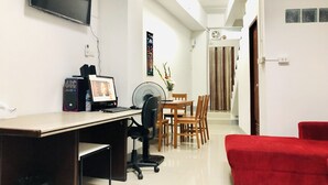 Un bureau à domicile avec un bureau, un ordinateur et une chaise. On aperçoit également un coin repas avec une table et des chaises. Un canapé rouge est visible au premier plan.