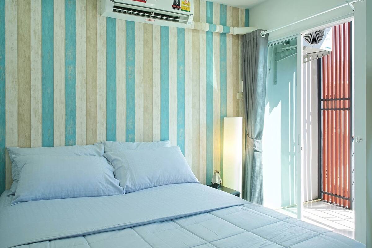 Hotelkamer met een bed, gestreept behang, een airconditioning en een schuifdeur, met uitzicht op buiten.
