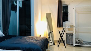 Une chambre d’hôtel avec un lit, un grand miroir, une lampe sur pied, une fenêtre avec des rideaux et une étagère blanche sur laquelle sont posés divers objets.